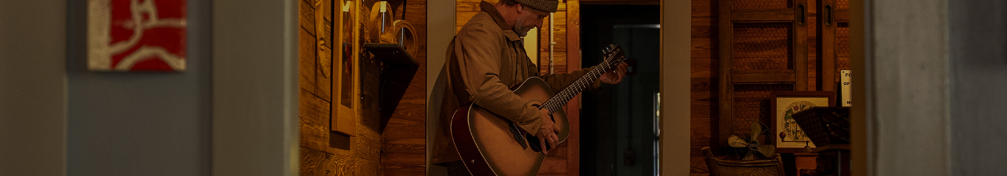 Musician playing acoustic guitar in rustic hallway with warm lighting