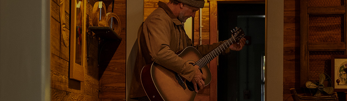 Musician playing acoustic guitar in rustic hallway with warm lighting