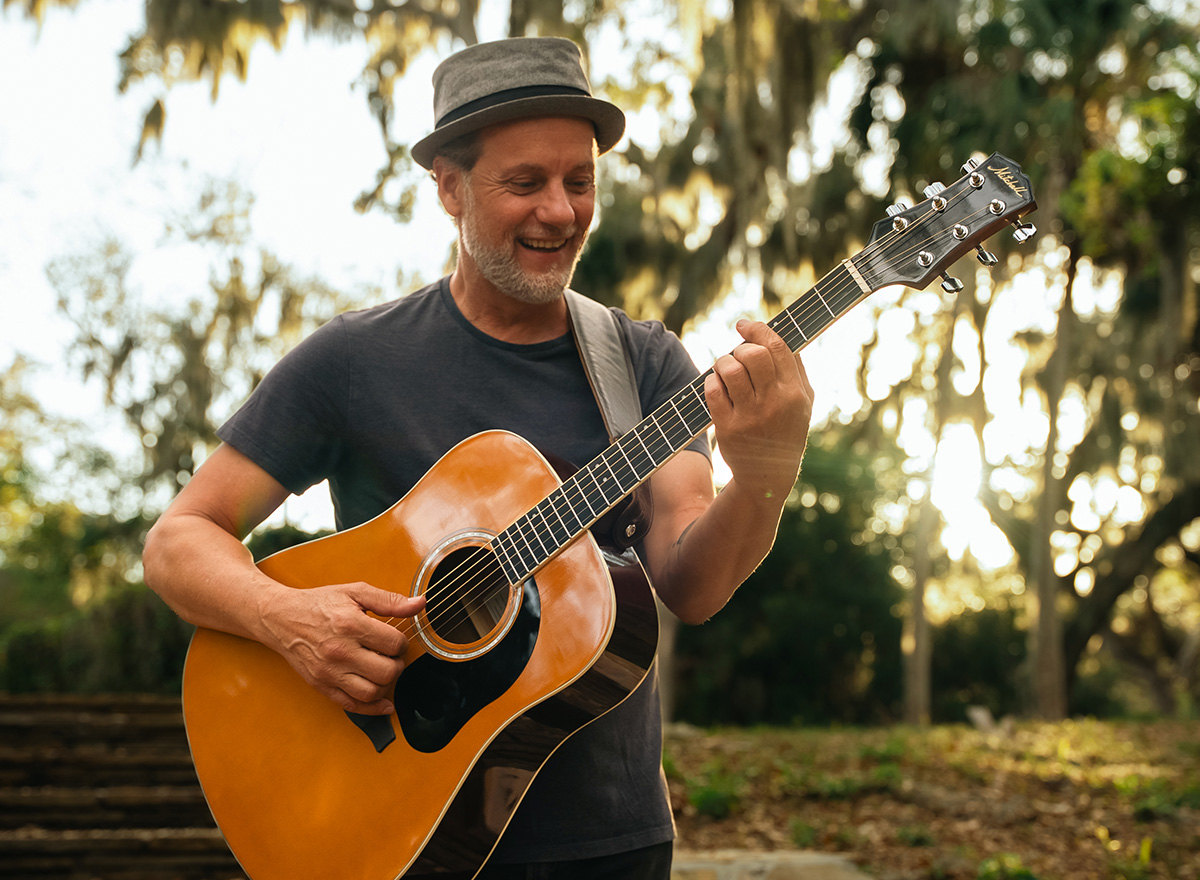 Man playing Mitchell acoustic guitar in sunlit park setting