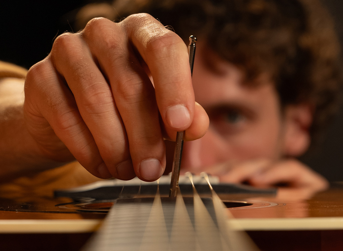 Close-up of hand adjusting acoustic guitar bridge pin
